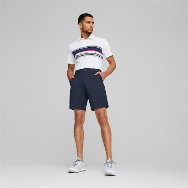 Against grey, a model poses in a white striped shirt, navy shorts, and trainers.
